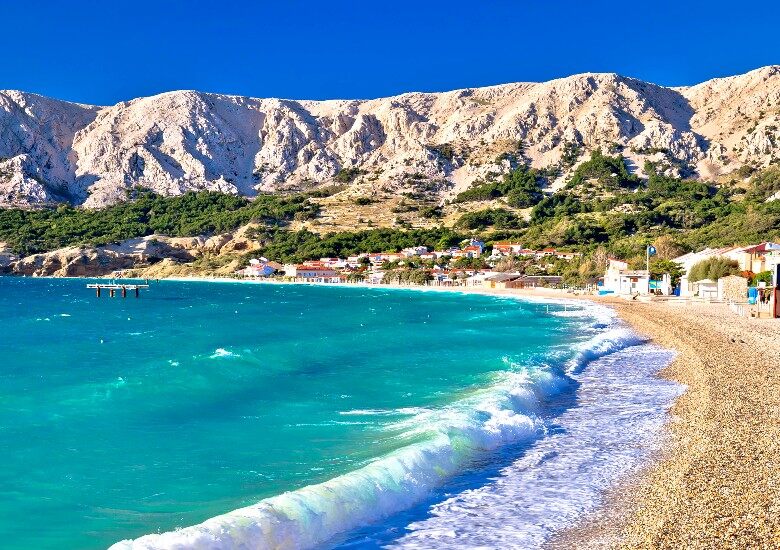 View of Baska Beach on Krk Island with turquoise water, pebbles, and surrounding cliffs.